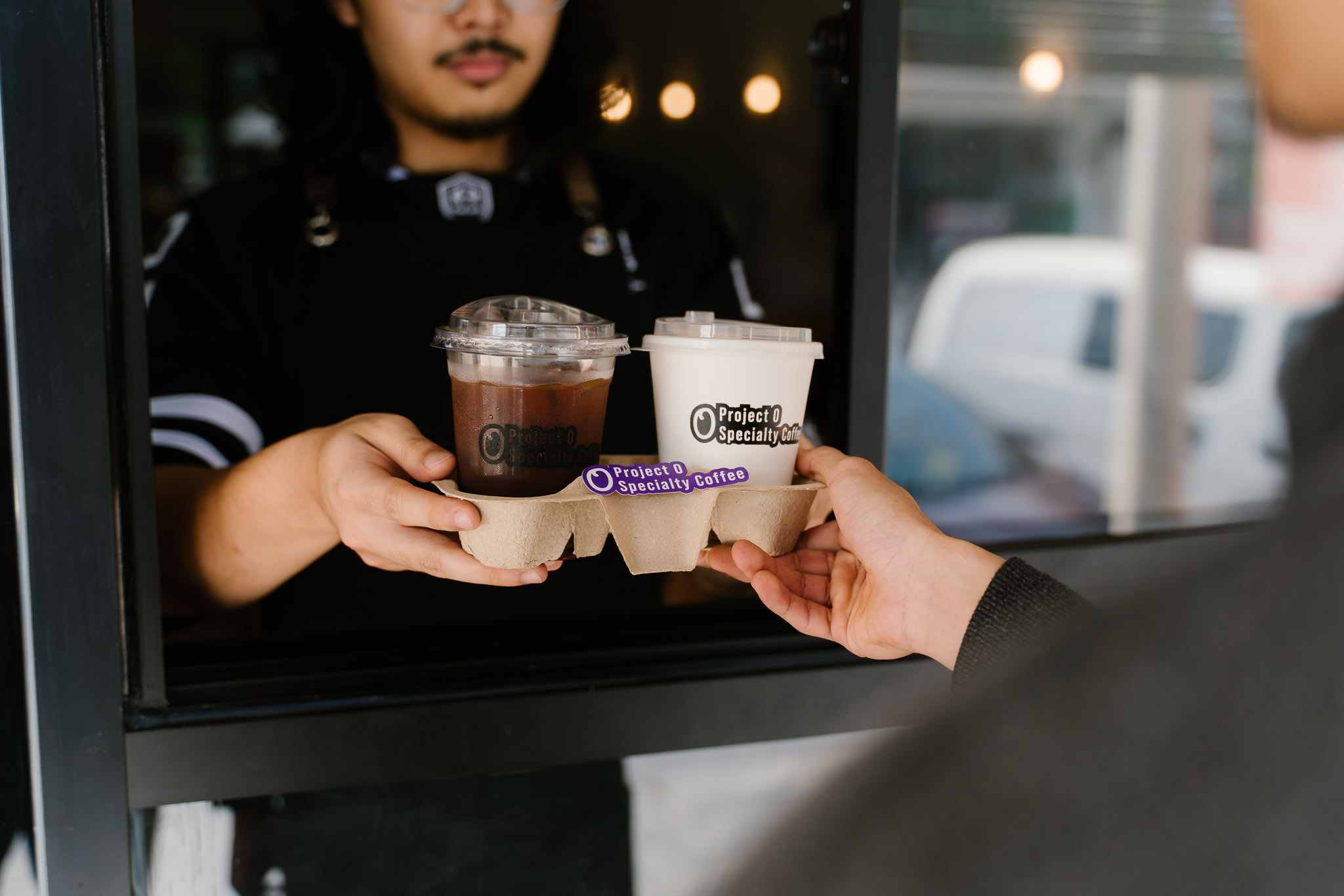A barista handing freshly brewed coffee to a customer at the walk-up window